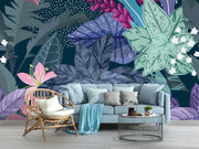 Illustrated tropical botanical wall mural with large jungle leaves, pink lilies, white flowers, and deep blue background, styled in a modern living room.