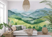 Watercolor green hills wall mural featuring lush rolling landscapes and soft blue mountains, styled in a cozy modern living room with a sofa.