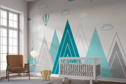 Modern geometric mountain wall mural in teal and grey with hot air balloons and clouds, styled in a contemporary nursery.