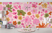 Vibrant floral wall mural featuring pink, orange and green abstract flowers, decorating a children’s playroom with a swing chair, pastel decor, and toy-filled storage.