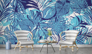 Tropical blue leaf wall mural featuring bold illustrations of large leaves in vibrant aqua and navy tones, decorating a living room.