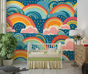 Bold and colorful rainbow wall mural with pink clouds and blue background, behind a white crib in a nursery setting.