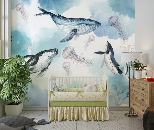 Underwater ocean wall mural with watercolor whales, jellyfish, and coral reefs in calming blue tones, displayed in a children's room with cozy decor.