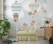 Nursery wall mural with pastel-colored forest animals flying in hot air balloons, surrounded by trees, clouds, and heart-shaped balloons