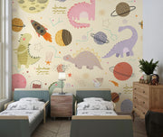 Children's room with Dino Galaxy Wall Mural featuring whimsical dinosaurs, rockets, planets, and stars in pastel colors, creating a magical space-themed decor.