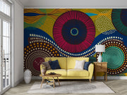 Vibrant abstract wall mural with bold geometric circular patterns, featuring bright colors and dynamic designs for modern interior decor. Styled in a living room with yellow sofa.