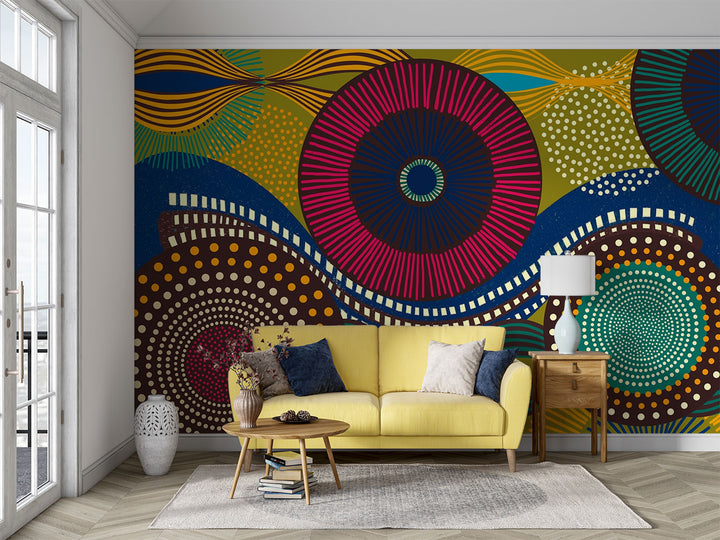 Vibrant abstract wall mural with bold geometric circular patterns, featuring bright colors and dynamic designs for modern interior decor. Styled in a living room with yellow sofa.