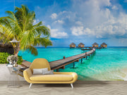Tropical paradise wall mural with overwater bungalows, palm trees, turquoise sea, and a wooden pier, creating a serene and exotic room atmosphere.