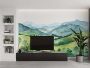 Watercolor green hills wall mural featuring lush rolling landscapes and soft blue mountains, styled in a cozy modern living room.