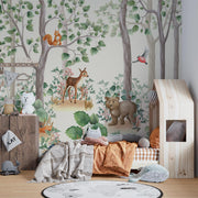 Woodland-themed wall mural featuring a bear cub, deer, squirrel, birds and lush green trees, decorating a cozy children's bedroom with a wooden house bed and natural decor.