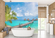 Tropical paradise wall mural with overwater bungalows, palm trees, turquoise sea, and a wooden pier, creating a serene and exotic room atmosphere.