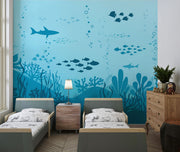 Underwater-themed wall mural featuring silhouettes of sharks, fish, and coral reefs in varying shades of blue, perfect for a calming and playful kids’ room.
