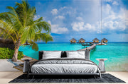 Tropical paradise wall mural with overwater bungalows, palm trees, turquoise sea, and a wooden pier, creating a serene and exotic room atmosphere.