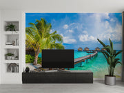 Tropical paradise wall mural with overwater bungalows, palm trees, turquoise sea, and a wooden pier, creating a serene and exotic room atmosphere.