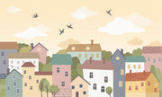 Whimsical village wall mural featuring pastel houses, trees, clouds, and flying birds, styled in a cozy and creative kids’ playroom.