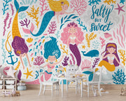 Colorful mermaid-themed wall mural in a children's playroom, featuring smiling cartoon mermaids with vibrant tails, sea creatures and coral.