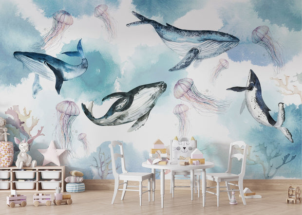 Underwater ocean wall mural with watercolor whales, jellyfish, and coral reefs in calming blue tones, displayed in a children's room with cozy decor.