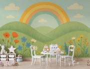 Children’s playroom featuring rainbow hill mural and white table with chairs and toy storage.