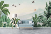 Scenic jungle wall mural with green tropical leaves, misty mountains, and flying cranes against a soft sunrise backdrop.