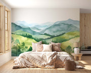 Watercolor green hills wall mural featuring lush rolling landscapes and soft blue mountains, styled in a cozy modern bedroom.