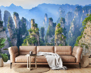 Zhangjiajie Mountain landscape wall mural featuring sandstone pillars, lush greenery, and misty peaks in a modern living room with natural decor.
