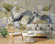 A sophisticated living room featuring an Elegant Heron & Lotus Pond Wall Mural with elegant birds in mid-flight, soft-toned lotus flowers, and floating lily pads. A neutral-colored linen sofa, wooden armchair, and decorative accents complete the serene, nature-inspired ambiance.