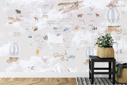 Whimsical world map wall mural featuring illustrated continents, animals, vintage aeroplanes, and hot air balloons, styled in a modern kids' room.