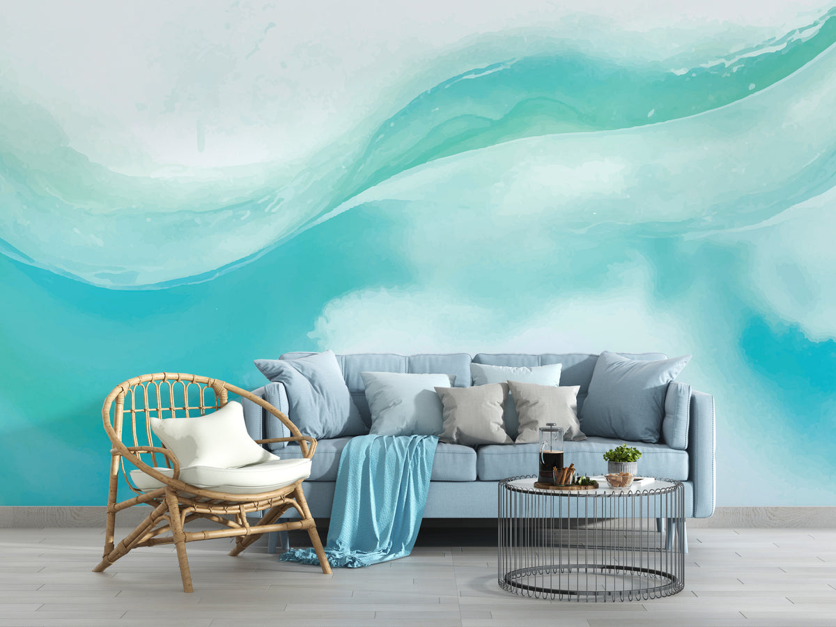 A modern living room setup featuring a large wall mural with an abstract wave design in shades of teal, turquoise, and white. In front of the wall is a light blue sofa with gray and blue pillows, a natural rattan armchair with a white cushion, and a round wire coffee table.