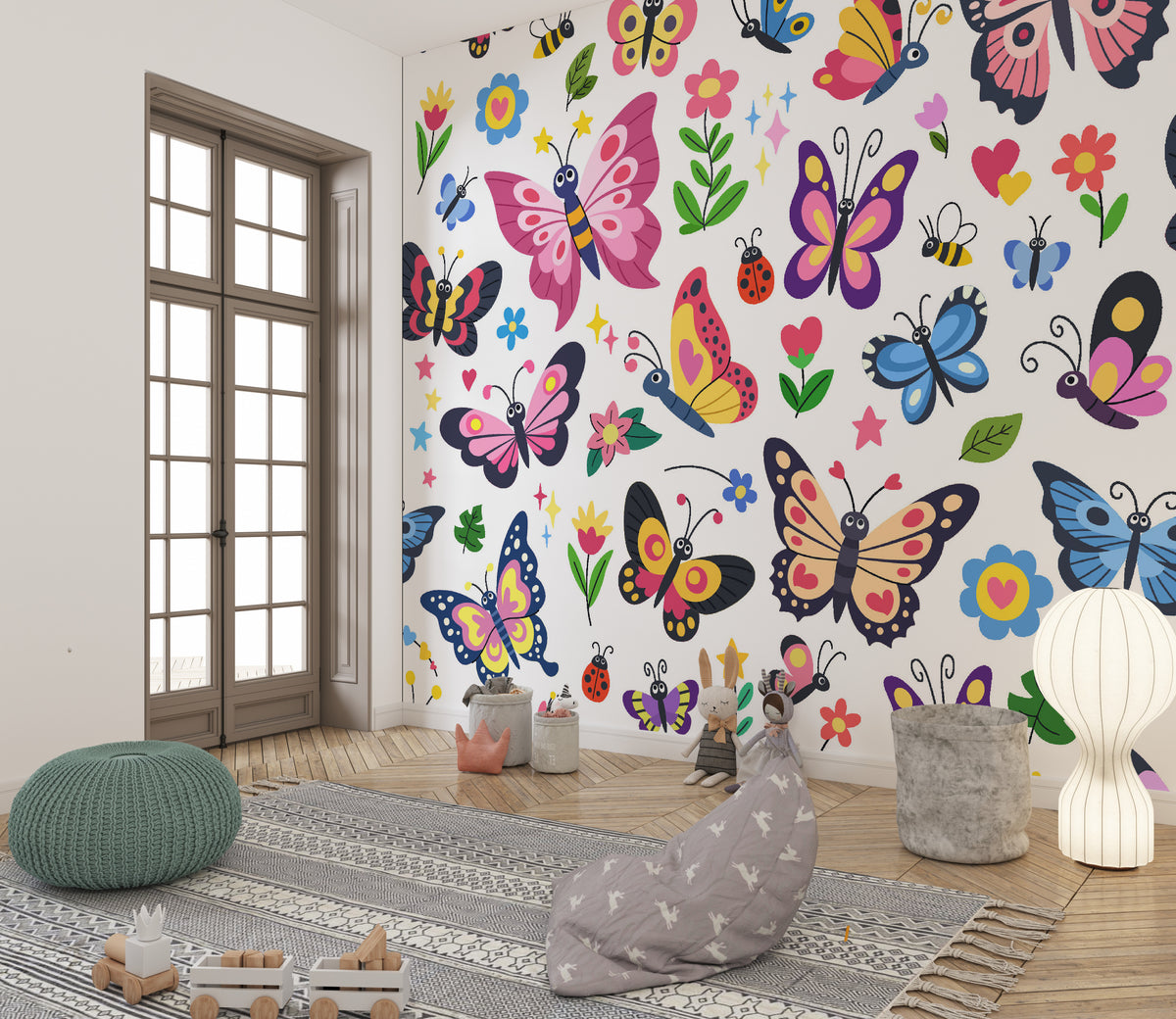 A colorful children's room featuring a wall covered in a whimsical butterfly and flower wallpaper mural. The room is styled with a gray patterned rug, a green knitted pouf, a gray bunny cushion, a white paper lantern lamp, and a wooden French door in the background.