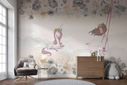 A whimsical nursery wall mural featuring a pink unicorn resting on clouds, a girl swinging with floral details, and soft pastel tones for a dreamy ambiance.
