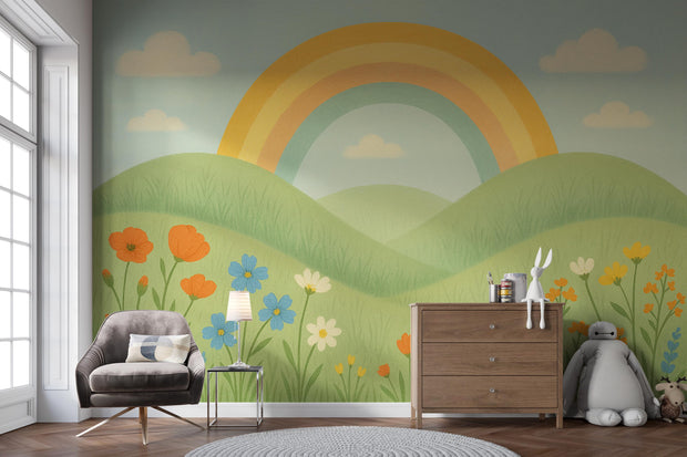 Rainbow-themed mural with soft hills and wildflowers, beside a modern wooden dresser and toys in a kids' room.