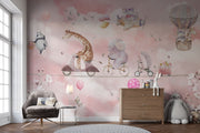 A whimsical nursery wall mural featuring playful animals, including a giraffe on a scooter, an elephant on a bike, and a panda floating with balloons over pink clouds.