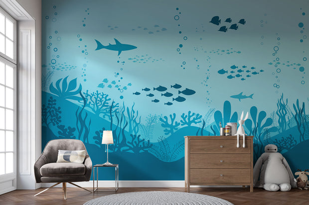 Underwater-themed wall mural featuring silhouettes of sharks, fish, and coral reefs in varying shades of blue, perfect for a calming and playful kids’ room.