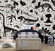 Black-and-white dinosaur-themed wall mural with skeletons, fossils, and "ROAR" text, decorating a kid's bedroom with a cosy bed, playful bedding and a modern lamp