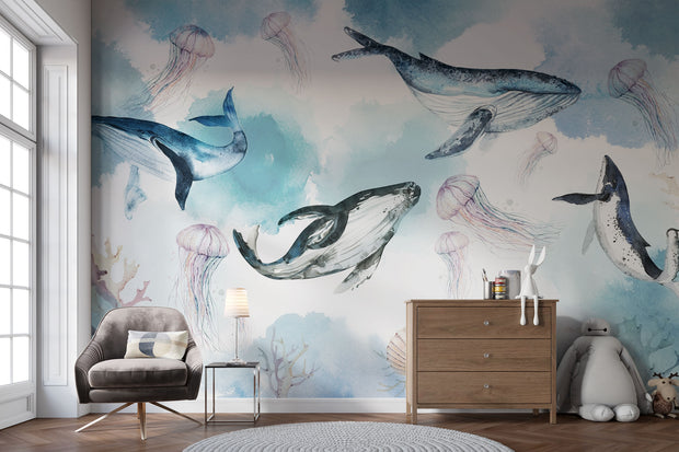 Underwater ocean wall mural with watercolor whales, jellyfish, and coral reefs in calming blue tones, displayed in a children's room with cozy decor.