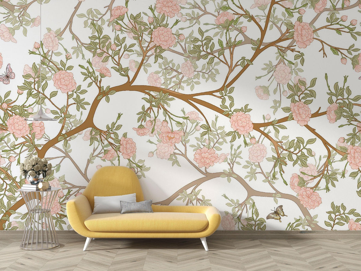 A styled interior scene showing a large wall mural with pink flowers and green leaves on brown branches, behind a yellow lounge chair and a small side table.