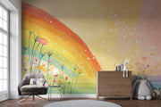 A colorful children's room featuring a large wall mural with a rainbow, wildflowers, and white speckles on a yellow-to-pink gradient background. The room includes a gray armchair, a wooden dresser with a white rabbit figurine, a stuffed animal, and a window on the left.