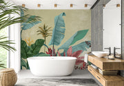 A modern bathroom interior featuring a large freestanding bathtub in front of a wall covered in tropical botanical wallpaper with oversized teal, green, and burgundy leaves on a warm beige background. A wood vanity with a white bowl sink, gray stone wall panels, and a potted plant are also visible.