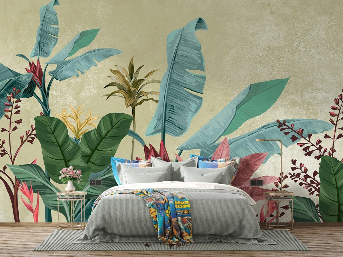 A styled bedroom featuring a large tropical wall mural with oversized blue-green banana leaves, palm trees, and red floral accents on a textured beige background. A gray bed with white bedding, colorful pillows, and a patterned throw blanket is centered in front of the mural.