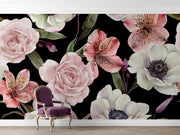 A floral wall mural featuring large pink and white flowers with green leaves on a black background, shown in a room setting with a purple velvet armchair and light wood flooring.