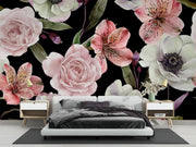 A modern bedroom setup featuring a bold floral wallpaper with large pink and white flowers on a black background. A low white platform bed with dark gray bedding is centered against the wall, flanked by two light wood nightstands with lamps and small decor.
