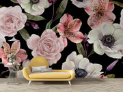 A large-scale floral wallpaper mural featuring pink, white, and green watercolor-style flowers on a black background, styled in a room setting behind a yellow modern lounge chair and a small wire side table.
