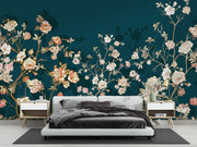 A modern bedroom featuring a large wall mural with an elegant floral pattern in soft pink, cream, and gold tones over a deep teal background. The room is styled with a low-profile white platform bed, matching bedside tables, and neutral-toned decor.
