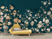 A yellow modern lounge chair with white legs placed in front of a dark teal wall covered in an ornate floral wallpaper pattern with cream, pink, and peach blossoms.