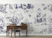 A styled interior room showing a large white wall covered in a detailed blue toile-style illustration mural. The scene includes a wooden desk, chair, books, lamp, birds, flowers, and figures within the printed design.