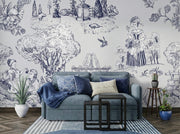 A styled living room featuring a light blue sofa with blue and cream pillows, set against a wall covered in a detailed blue and white toile-style wallpaper with illustrations of figures, trees, and animals. A striped rug, nesting black tables, and potted plants complete the scene.