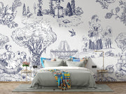 A styled bedroom featuring a large white wall mural with detailed black and blue botanical and figurative line art. A bed with gray bedding, blue accent pillows, and a colorful throw blanket sits in front of the mural, flanked by two small side tables with gold-framed lamps.