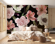 A large floral wall mural with oversized pink, white, and green flowers on a black background, installed behind a bed in a styled bedroom with wood flooring and light wood walls.