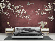A modern bedroom featuring a large wall mural with white cherry blossom branches and a bird on a textured dark red background, styled with a low white platform bed, matching nightstands, and lamps.