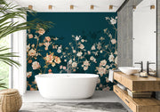A modern bathroom interior featuring a dark teal floral wallpaper mural behind a freestanding white bathtub, with a wood vanity, vessel sink, mirror, and a potted plant at the side.